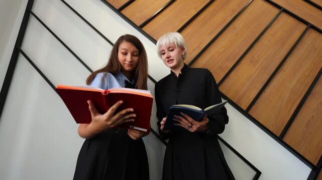 Two students stand side by side in a modern learning space, smiling while reviewing notes together,