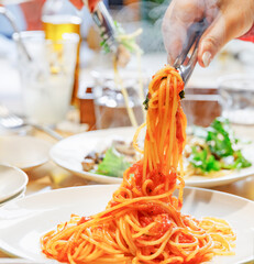 トングで高く持ち上げられた湯気が立つ熱々のトマトソーススパゲッティ