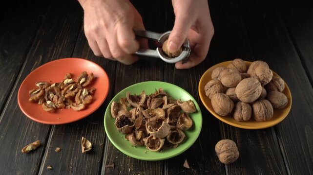 Hands cracking walnuts with a nutcracker, revealing the nut inside while surrounded by empty shells and shelled nuts on colorful plates