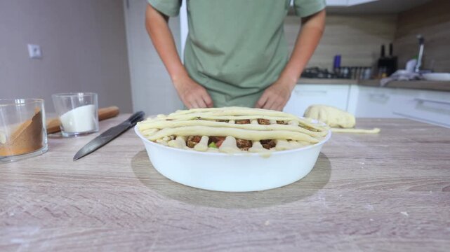 A baker weaves thin dough strips over a filled apple pie in a lattice pattern, meticulous, hands-on finishing for a classic homemade dessert.