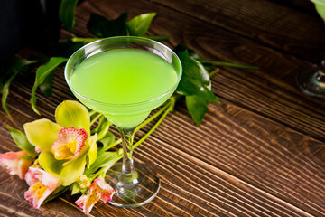 A vibrant green cocktail in a martini glass, elegantly placed beside delicate orchid flowers on a bamboo mat, evoking a tropical and refreshing ambiance. © zulfiska