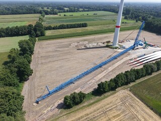 A lattice boom crawler crane awaits the assembly of a new wind turbine in the wind farm  aerial view, preparation, construction site, energy transition © keBu.Medien