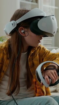 Caucasian child girl using vr technology for hobby entertainment daughter kid in virtual reality headset glasses helmet holding controllers playing virtual modern video game in metaverse at home couch