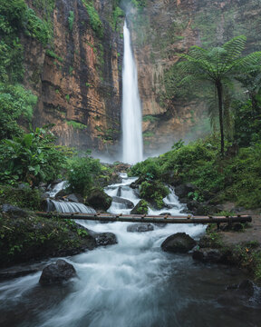 Aerial view of the dramatic Coban Rondo Waterfall cascading down rugged cliffs amidst a verdant jungle, Pujon, Jawa Timur, Indonesia.