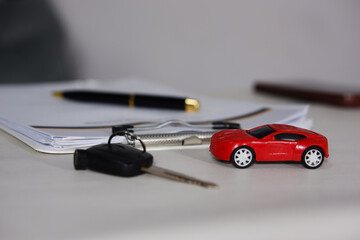 Miniature vehicles and keys, along with a clipboard containing documents, are on a work desk. Insurance, vehicle rentals, and vehicle sales.
