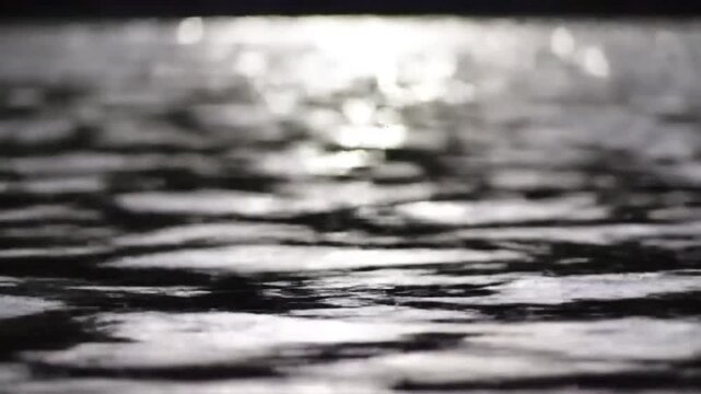 Abstract dark water surface with shimmering light reflections. Rippled liquid texture at dusk or dawn, creating a tranquil and moody background.