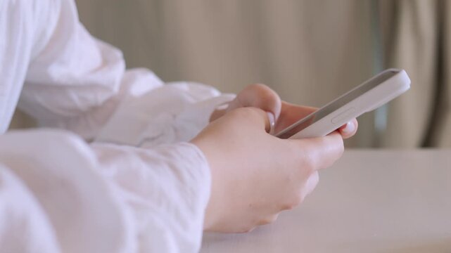 Woman is holding a cell phone in her hand. She is looking at the screen. The phone is white