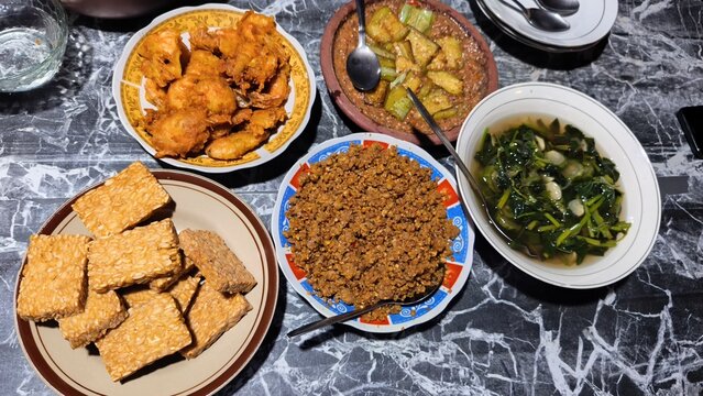 Assorted Indonesian traditional dishes including fried tempeh, prawns, sambal, and saut&eacute;ed vegetables.