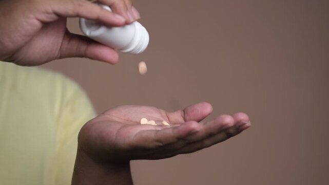 close-up of a person pouring tablets from a small medicine bottle into open palm, showing medication dose, healthcare routine, and supplement use