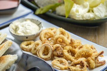 A plate of crispy fried squid rings with tartar sauce.