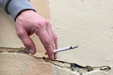 Hand holding a lit cigarette against a cracked, textured wall