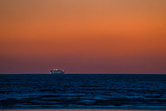 View of a distant ship cutting through the dark waters under a gradient sky ablaze with fiery oranges and deep purples, Karachi, Sindh, Pakistan.