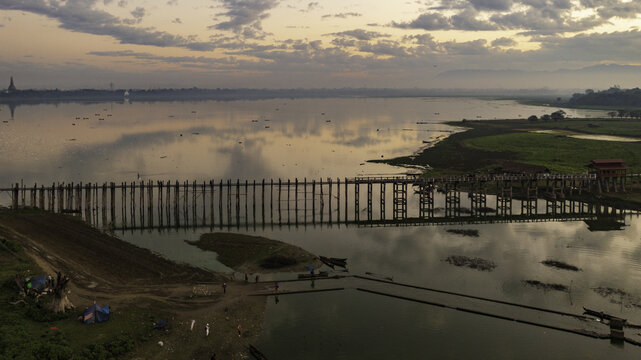 Aerial view of the U Bein Bridge stretching across the tranquil Taungthaman Lake, reflecting the soft hues of dawn, Mandalay, Mandalay Region, Myanmar.