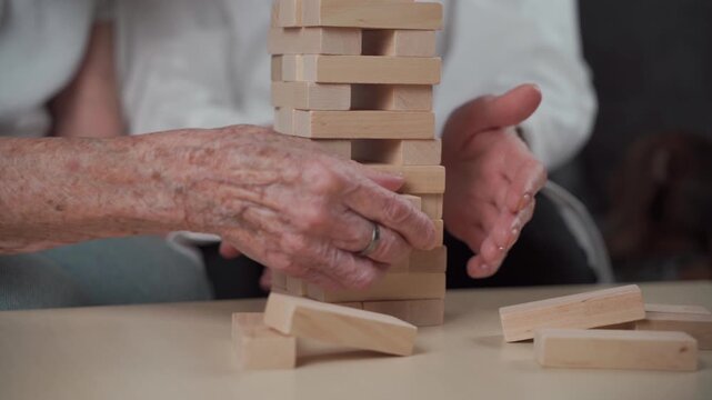Senior woman practice skills build wooden blocks, building tower and trying not to let it fall, game. Old patient pull out block, place on top, support dotor during therapy dementia in house.