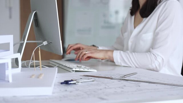 Architect creating new designs, working at a computer in office with blueprints and drafting tools. Business and architecture concept