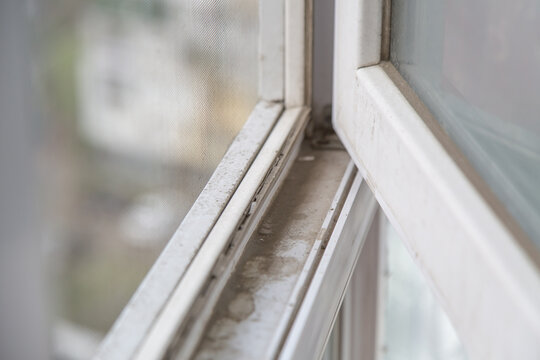 Dirty plastic window frame and sill with dust and stains, viewed through mesh screen with blurred city background, symbolizing neglect and cleaning need, concept of home hygiene