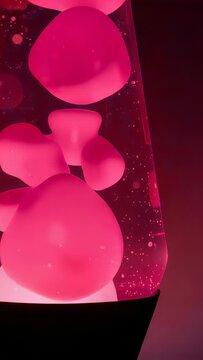Vertical video: Internal bulb heating lava lamp column, pink wax blobs bulging and rising in corner