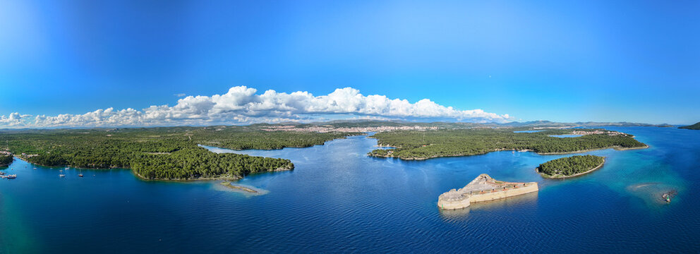 Aerial view of the historic St Nicholas' Fortress standing guard amidst the azure sea, surrounded by green islands and a clear sky, Sibenik, Croatia.
