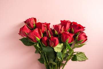 Fototapeta premium Valentine's Day background. Red roses flowers in heart shaped bouquet over pink background. Abstract flat lay. Celebrate, festive greeting card.