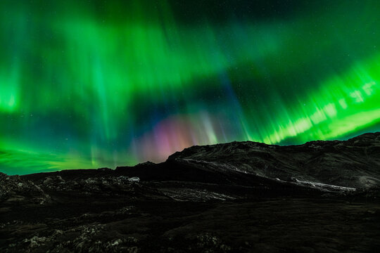 View of the Northern Lights dance with vibrant green and subtle purple hues above a stark, dark landscape under a starlit sky, Kleifarvatn, Grindavikurbaer, Iceland.