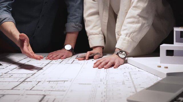 Architects and engineers collaborating on a new building project, planning structural details and design concepts using blueprints and a scaled architectural model on a desktop