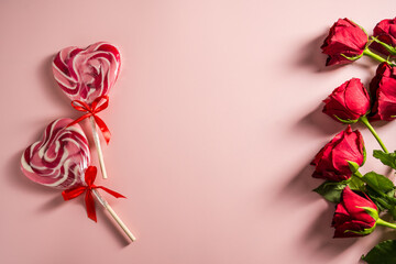 Valentine's Day background. Red roses and heart shaped lolly candy over pink background. Abstract flat lay. Celebrate, festive greeting card.
