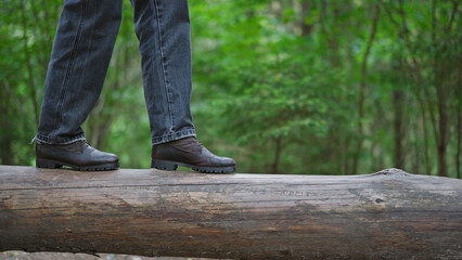 Woman hiker in boots balances on a fallen tree trunk in forest. Person walking, taking steps, step by step.