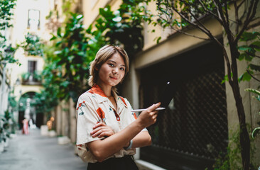 Fototapeta premium Asian woman with stylus and tablet crosses arms confidently, looking at camera, embodying digital independence, professionalism, and the strength of remote technology.