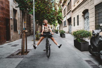 Naklejka premium Woman on bicycle stretches both legs forward while riding, headphones on, smiling brightly. Portrays joy, freedom, and playful interaction with mobile technology in modern freelance life.