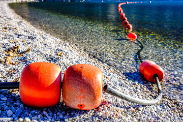 Buoys line the shore of a lake guiding boats along the water as the sun shines down on the clear...