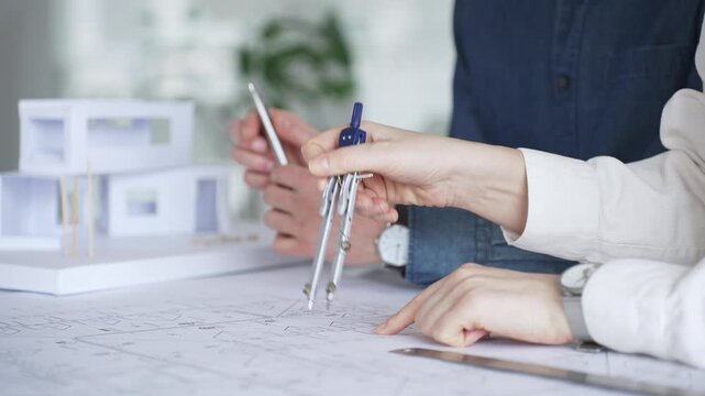 Architects collaborating on blueprint plans, discussing engineering details and project designs, planning construction development with a laptop in a modern office environment