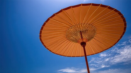 Orange parasol offers shade against a bright blue sky viewed from below