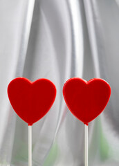Minimalist composition featuring two red heart-shaped lollipops on a soft fabric background. The clean design and balanced symmetry make this image ideal for graphic design projects, website headers, 