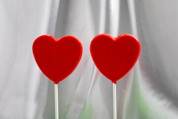 Minimalist composition featuring two red heart-shaped lollipops on a soft fabric background. The clean design and balanced symmetry make this image ideal for graphic design projects, website headers, 