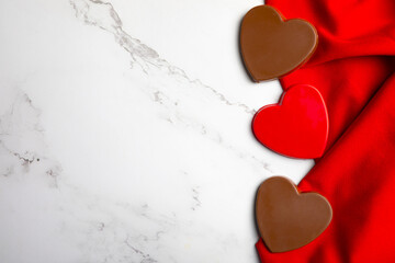 Heart-shaped chocolate candies arranged on rich red fabric over a white marble background with ample copy space. This clean and elegant composition is ideal for Valentine&rsquo;s Day promotions