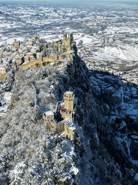 Aerial view of the snow-dusted Guaita fortress perched atop Monte Titano, a stark contrast against the soft, diffused light, San Marino, San Marino.