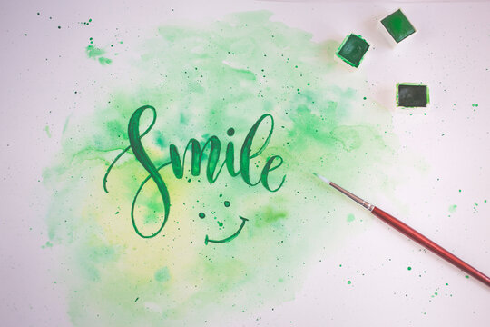 Close-up of the word smile and a smiley face painted on a piece of paper with green paint and a paintbrush