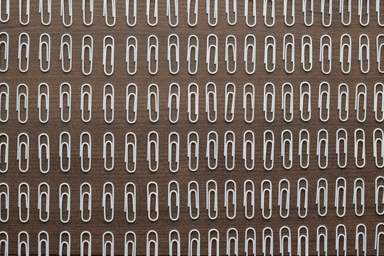 Many white paper clips on wooden table. Concepts of order obsession . Metaphor of ordinary people in society.