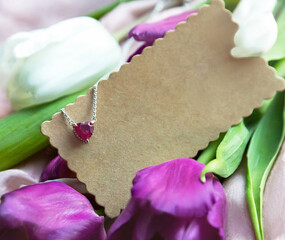 Jewelry. Metal chain with stylish pink heart pendant on fresh flowers It creating romantic atmosphere. Valentine's day, mother's, woman;s day, love holidays. Copy space, empty place on  card.