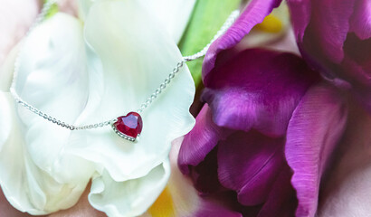 Jewelry. Metal chain (necklace) with stylish pink heart pendant on fresh flowers (tulip). It creating, tender, romantic atmosphere. Valentine's day, mother's, woman's day, love holidays.