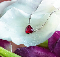 Jewelry. Metal chain with stylish pink heart pendant on fresh flowers with dew drops. It creating, tender, romantic atmosphere. Valentine's day, mother's, woman's day, love holidays.