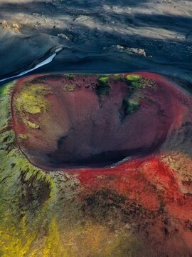 Aerial view of a volcanic crater with vibrant hues of red, green, and yellow contrasting against the dark, textured earth, Akureyri, Rangarthing ytra, Iceland.