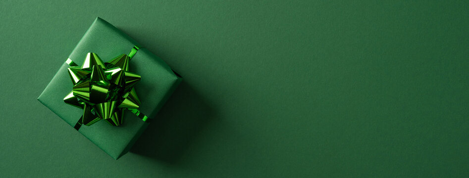A green gift box with a glossy bow sits on a deep green banner background, conveying luck, Irish charm, and a festive greeting for St Patrick's Day celebration