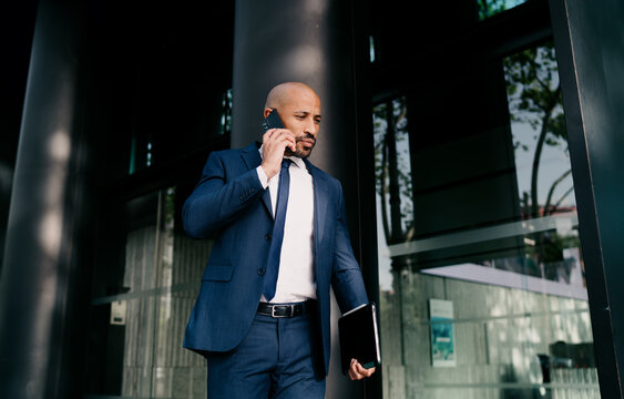 Businessman walks confidently outside building while on phone, representing mobile entrepreneurship and digital agility in fast-paced business communication.