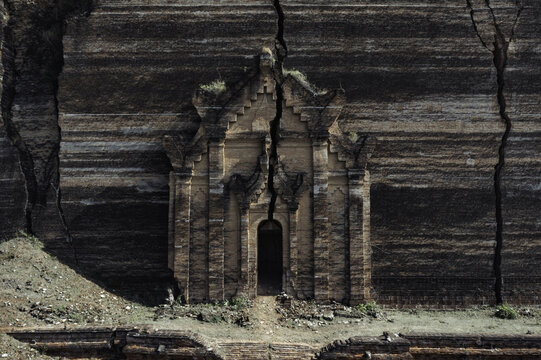 Aerial view of a weathered brick temple, nestled against a striated cliff face, split by deep fissures, Old Bagan, Mandalay Region, Myanmar.