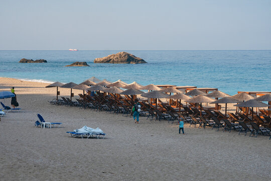 View of endless rows of straw umbrellas and beach chairs line the golden sands meeting the turquoise sea under a clear sky, Lefkada, Greece.