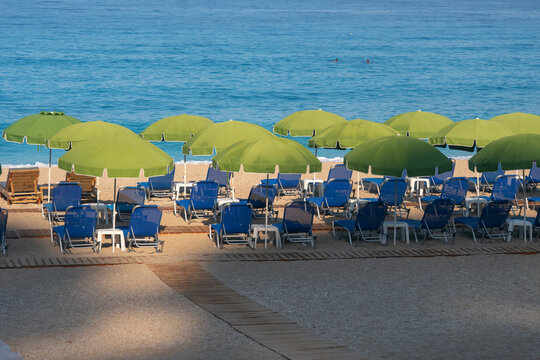 View of rows of bright green umbrellas create a playful contrast against the deep blue sea and sky, with blue beach chairs in Kathisma, Lefkada, Greece.