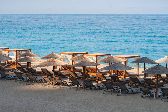 View of the beach with sun loungers under thatched umbrellas contrasting against the turquoise water, Kathisma beach, Lefkada, Greece.