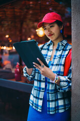 Young Asian woman reads tablet with playful frown, reacting emotionally to content, showing genuine digital engagement and human-tech connection in relaxed city scene. © BullRun
