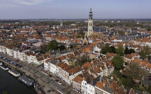 Aerial view of red-tiled roofs cascade towards the serene canal waters, punctuated by the towering spire of the Lange Jan, Middelburg, Zeeland, Netherlands.